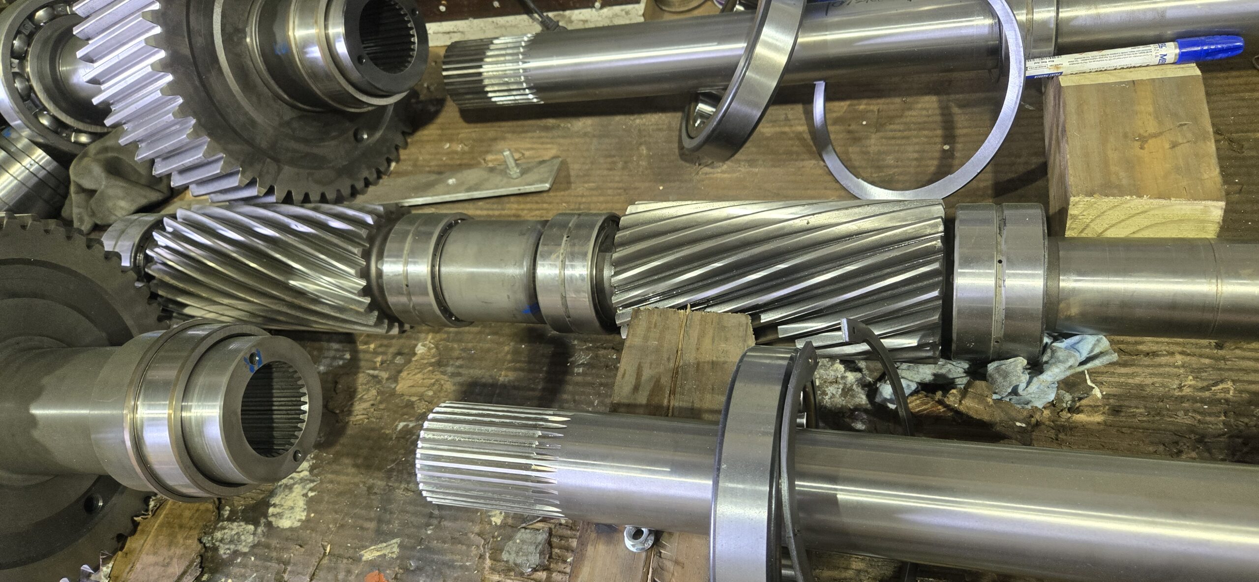 Disassembled high-precision helical gears and roller bearings from an industrial extruder gearbox being analyzed for wear and tolerances at Zala Machine Co.