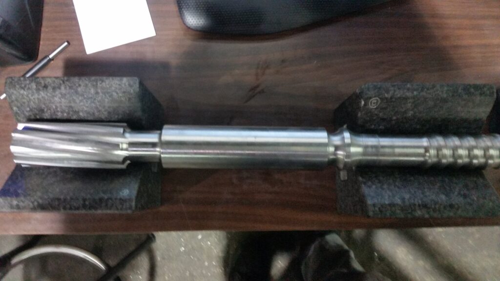 Finished screw shaft set on granite blocks, fluted drive end at one side and the flighted section at the other