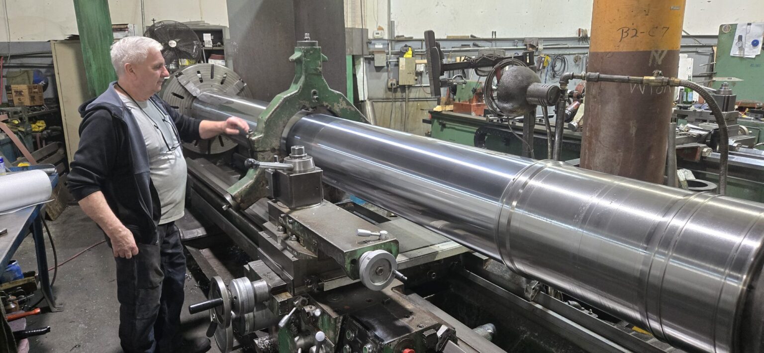 Machinist turning a long shaft on a large manual lathe