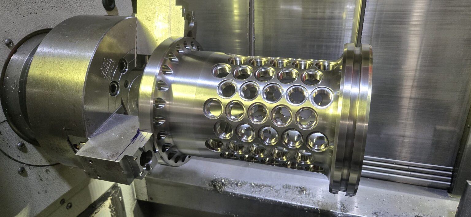 Titanium prototype cylinder in the CNC lathe, rows of radial holes drilled through the wall