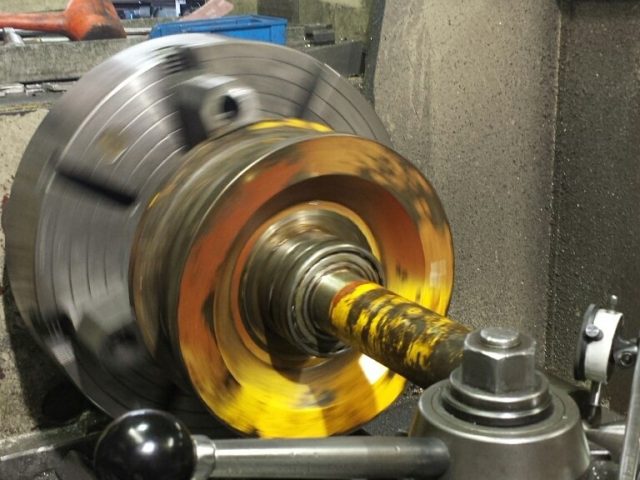 Bronze-faced disc turned in the lathe chuck, fresh cut showing bright against the bore