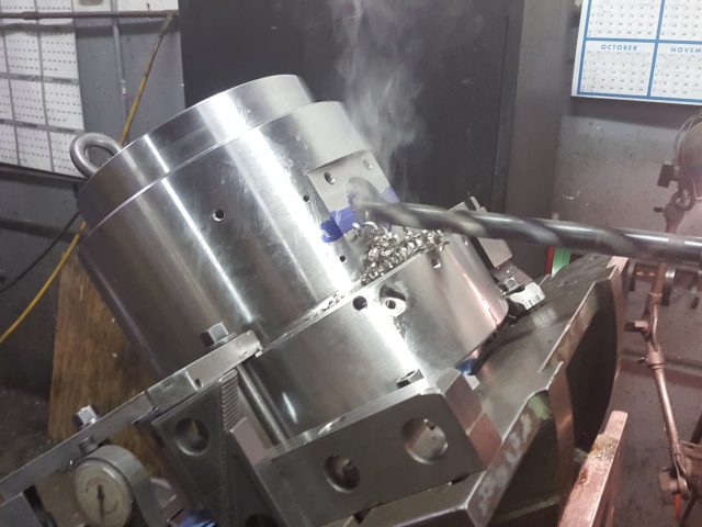 Large die body clamped on the tilting fixture, boring bar cutting with coolant steaming off the work