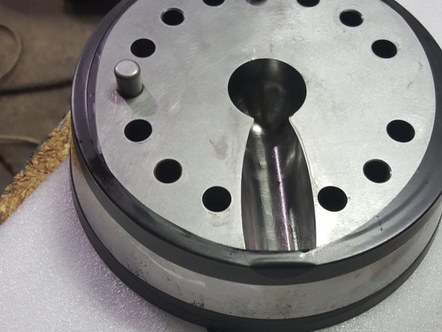 Die plate resting on packing foam, teardrop flow port and bolt circle machined into the face