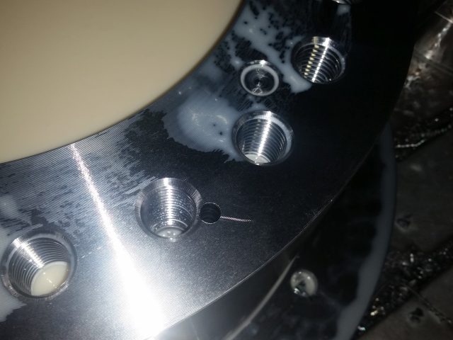 Tapped holes and counterbores machined into a large flange face, coolant still on the part