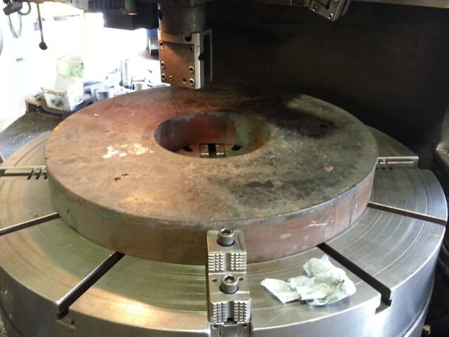 Large disc set on the vertical boring mill table, jaws closed on the rim before turning