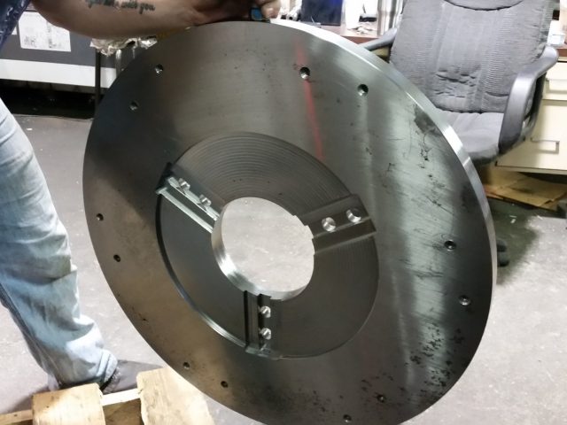 Machinist handling a large machined steel plate, centre bore opened and keyed inserts fitted