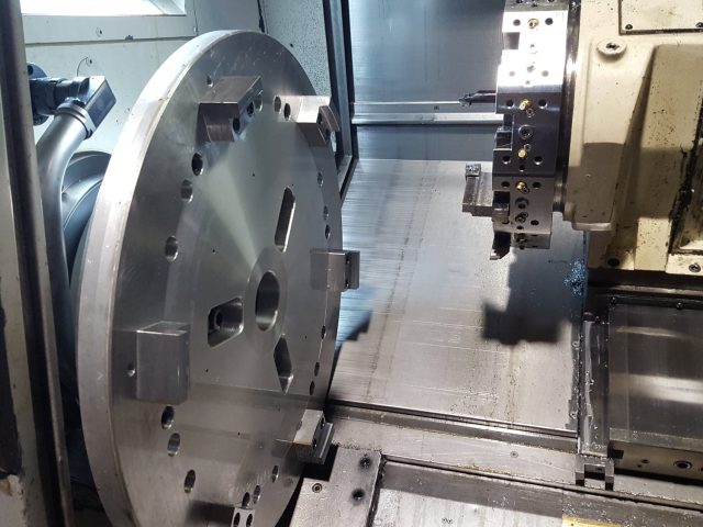 Large plate held in the chuck with pockets and holes milled through, tool head alongside