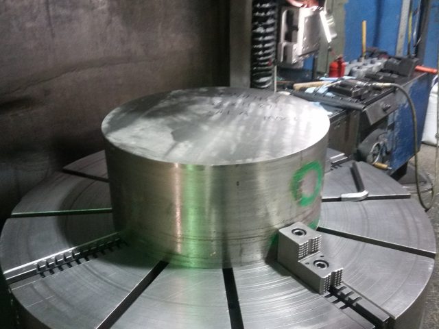 Large steel billet faced off on the boring mill table, jaws gripping the outside diameter
