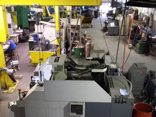Elevated view across the Zala Machine shop floor, CNC machines and benches under the yellow gantry crane