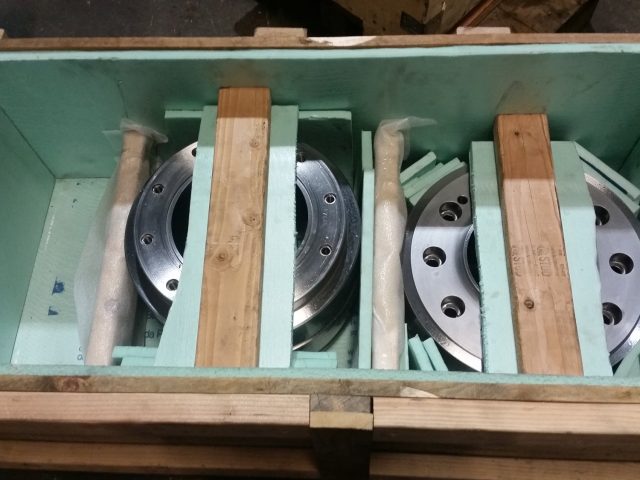 Two machined flange parts blocked upright in a lined crate, braced with timber for shipping