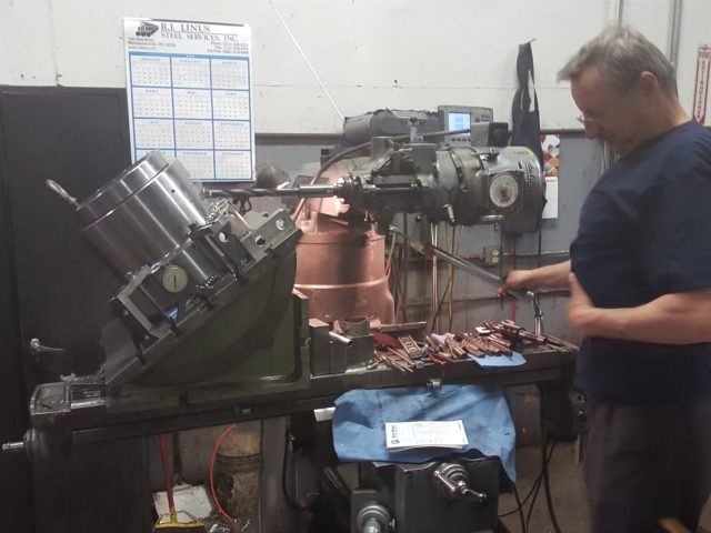 Machinist working at the bench with parts laid out beside the machine