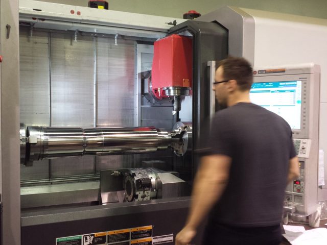 Machinist at the mill-turn control with an extruder screw running in the machine behind him