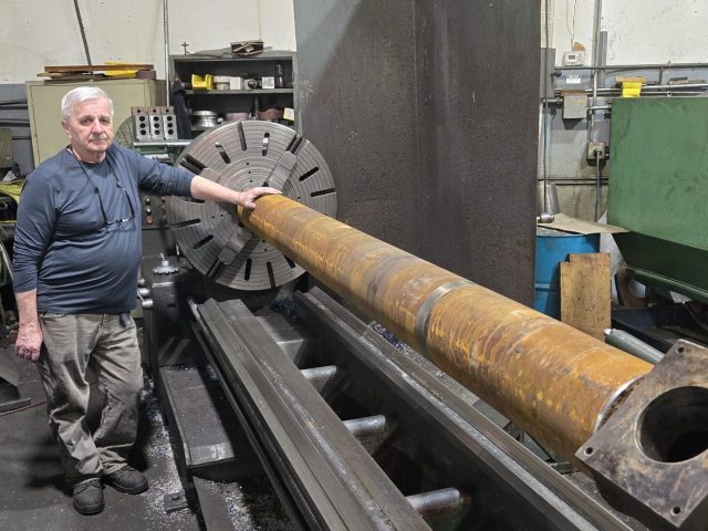 Machinist beside a long extruder barrel set up on the engine lathe