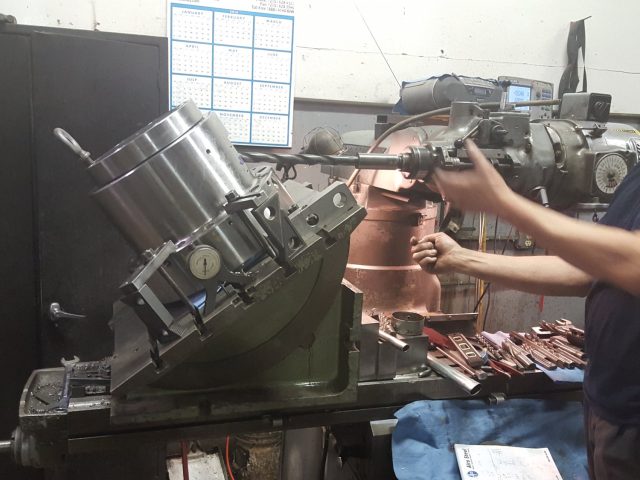 Machinist working on a large die body clamped in the tilting fixture, tooling laid out on the bench