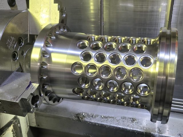 Titanium prototype cylinder in the CNC lathe, rows of radial holes drilled through the wall